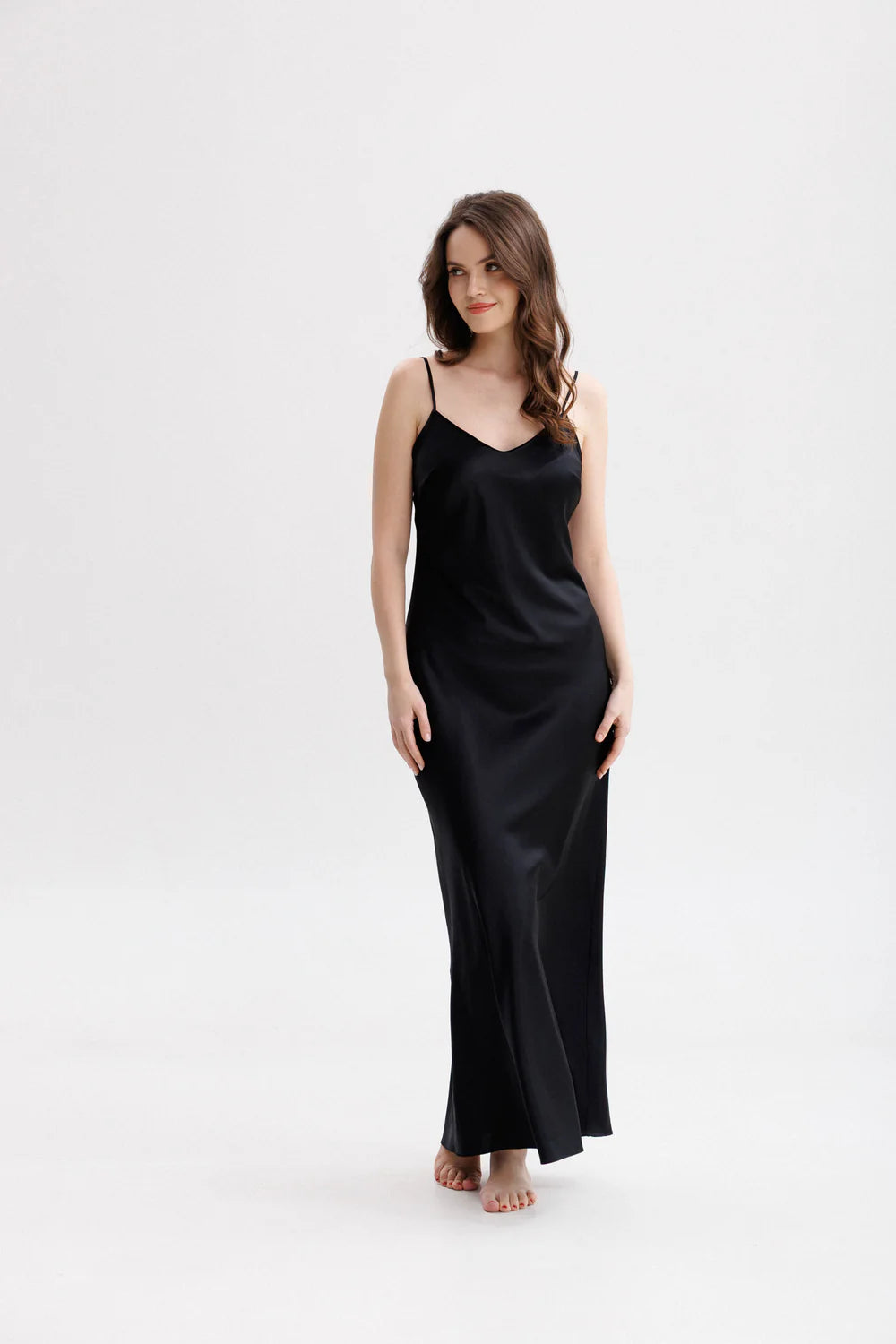 Woman wearing a long silk black slip dress on a spaghetti straps showing the front pose. 
