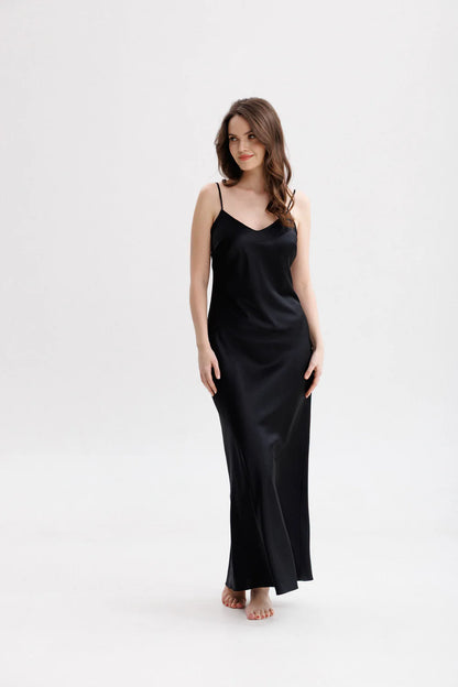 Woman wearing a long silk black slip dress on a spaghetti straps showing the front pose. 